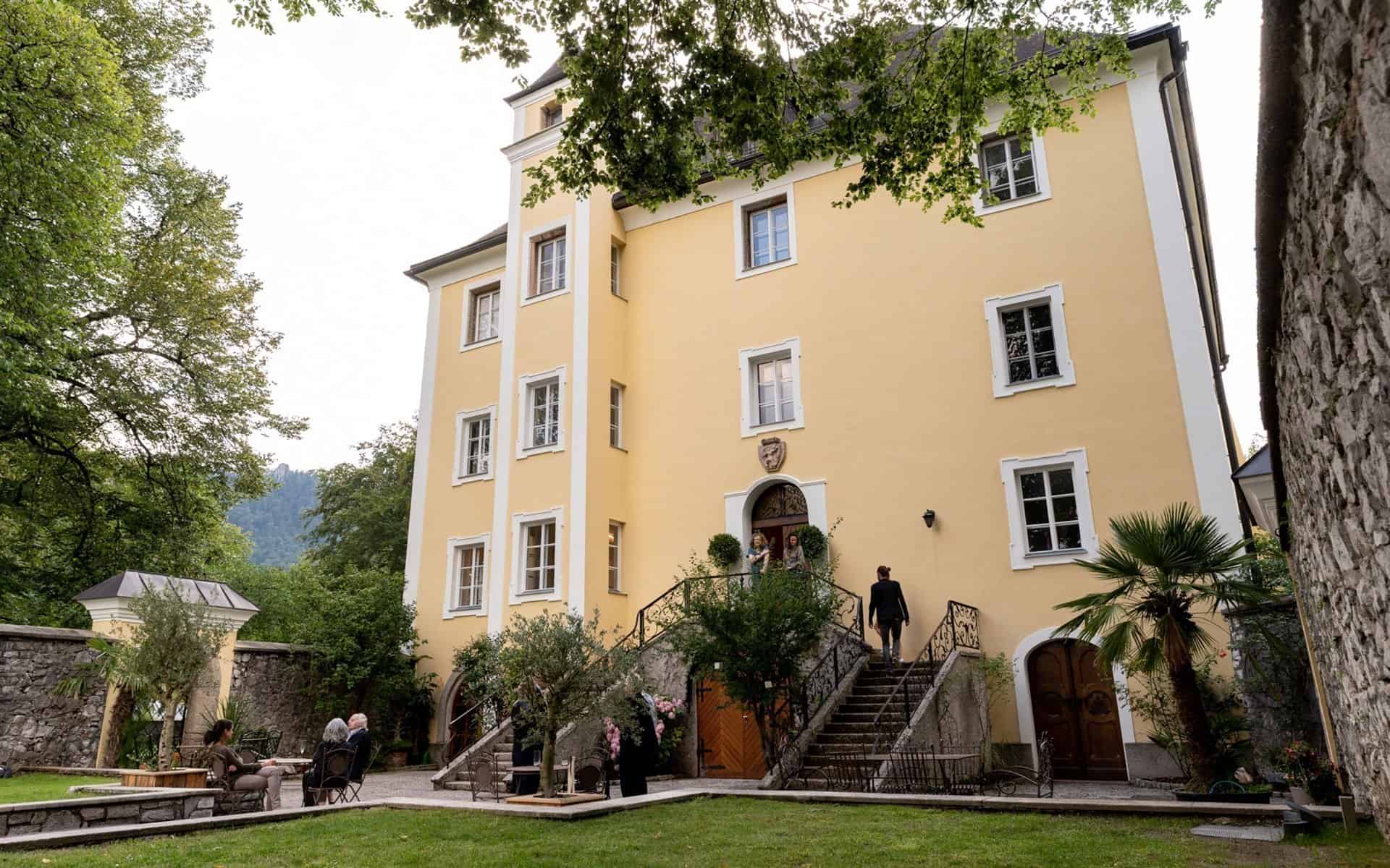 Schloss Wiespach in Hallein — Innenhof mit gelber Fassade, Freitreppe und Gästen am Sommerabend.